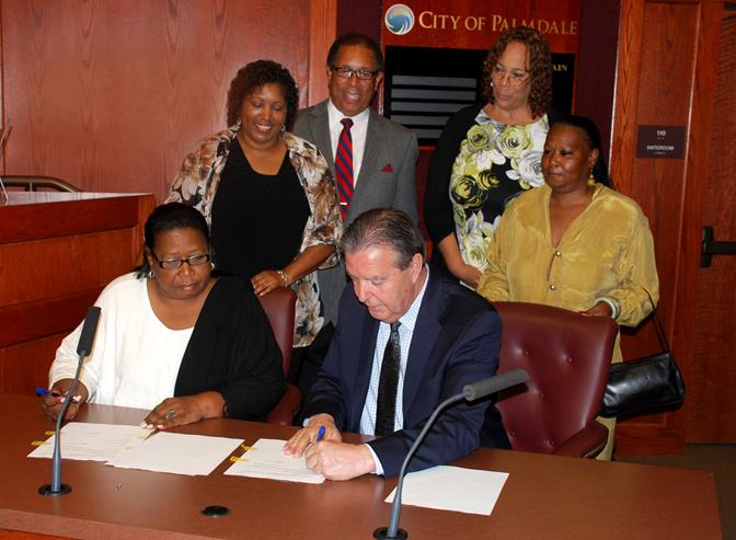 Caption: Sun Village Town Council President Magdalene Lawrence, left, and Palmdale Mayor Jim Ledford, right, sign the historic MOU. Looking on from left to right: Sun Village Town Council Secretary Bernadette Moore, Palmdale Councilmember Fred Thompson, Palmdale Deputy City Clerk Roxanne Faber and Sun Village Town Council  Assistant Treasurer Gem Lawrence. 