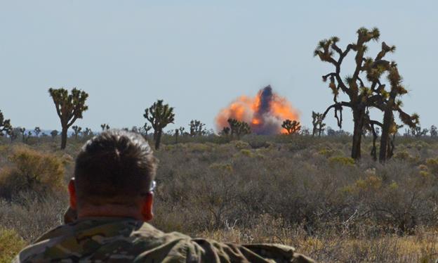 An Airman from the 812th Civil Engineering Squadron, Explosive Ordnance Disposal Flight, watches the fire ball as 15 gallons of nitrocellulose-dope lacquer is blown up with C-4 June 6. (U.S. Air Force photo by Kenji Thuloweit)